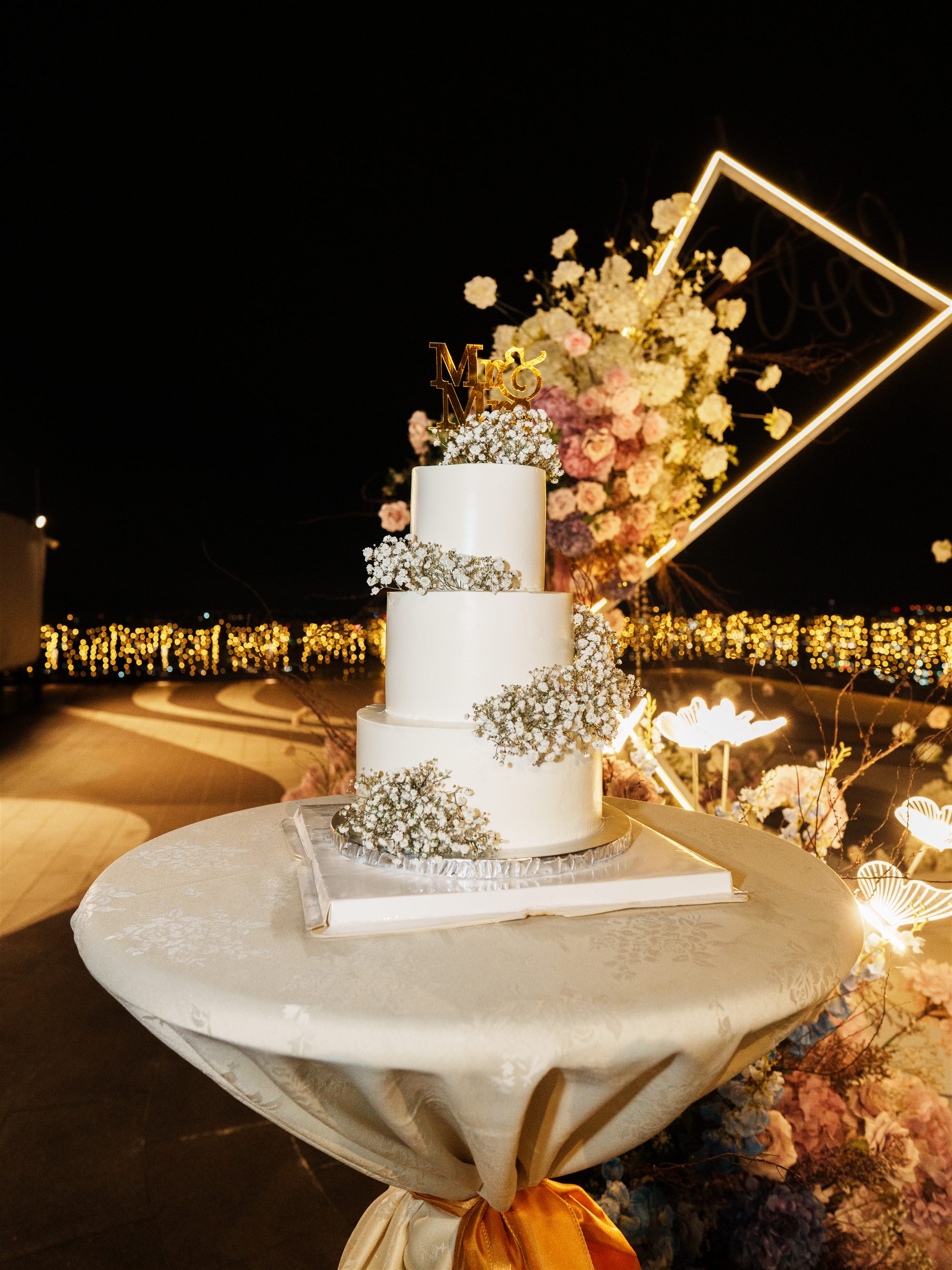 Three-tier wedding cake with floral arch and twinkling city lights