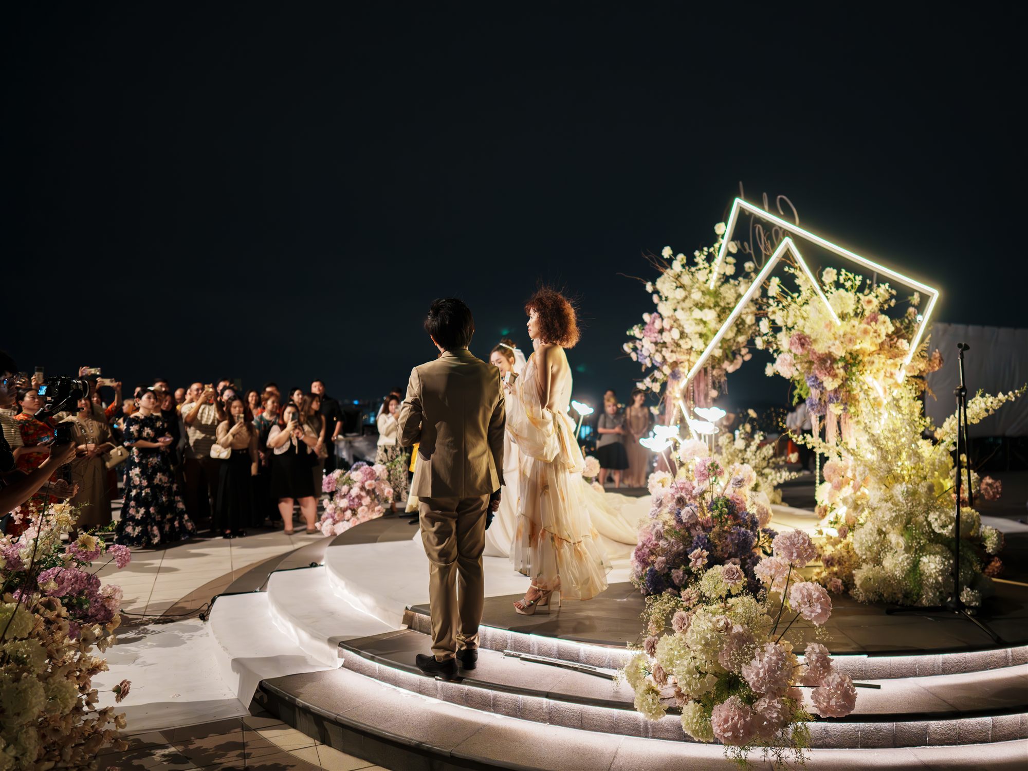Couple on stage with crowd watching at night wedding celebration
