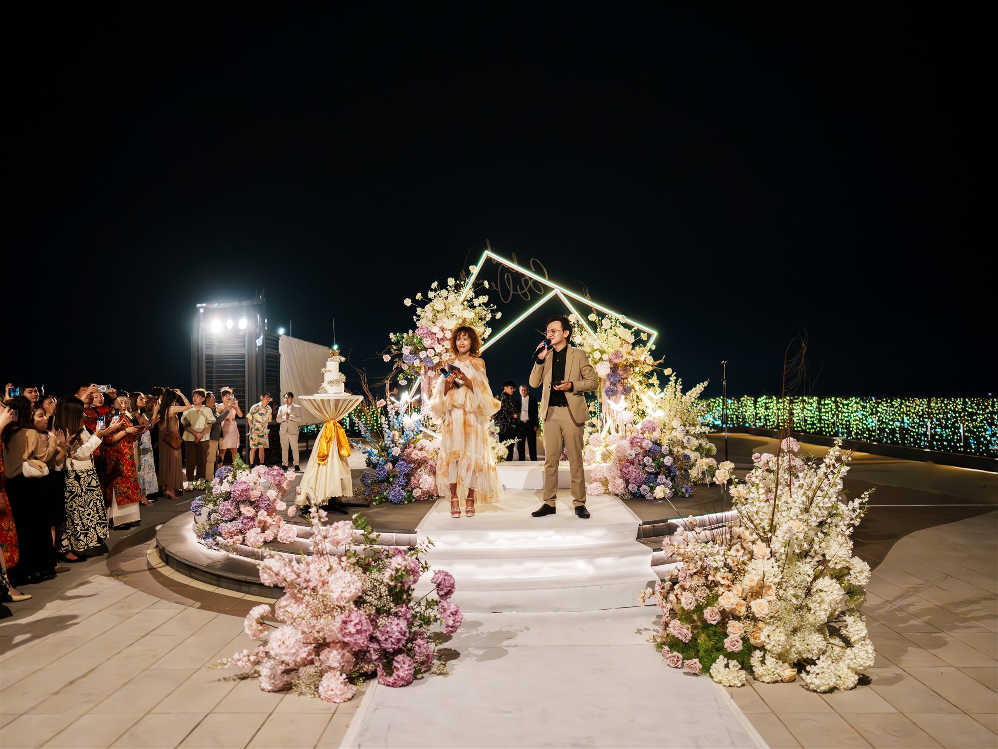 Night wedding ceremony at floral arch with guests and KL skyline backdrop