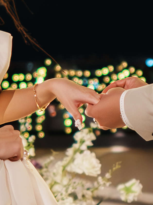 Close-up of couple holding hands at wedding ceremony with bokeh floral lights